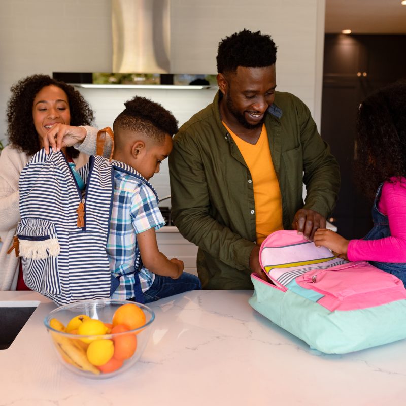 Happy african american parents and children preparing backpacks for school